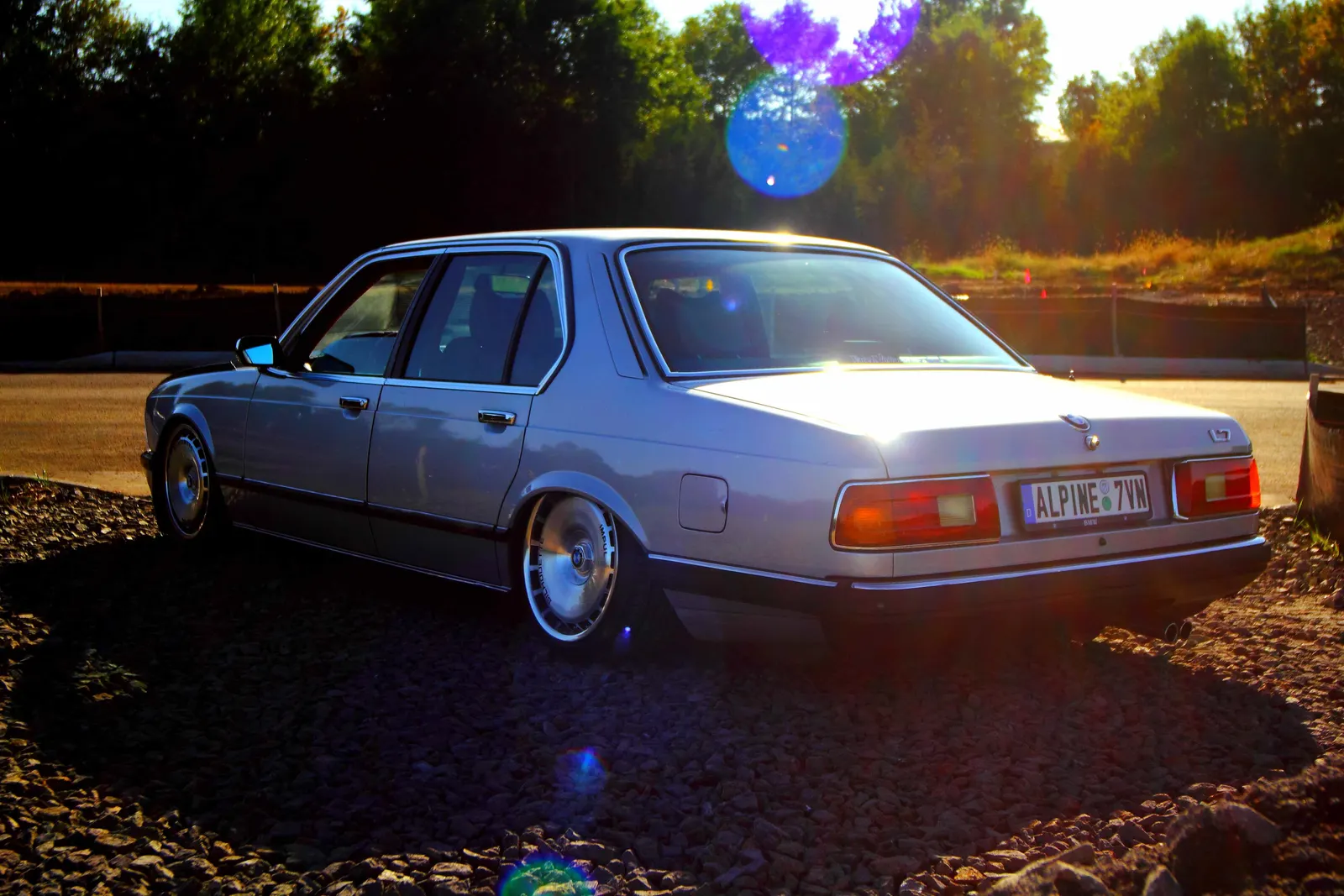 Silver BMW E23 L7 sedan sitting low on turbine-style wheels at sunset