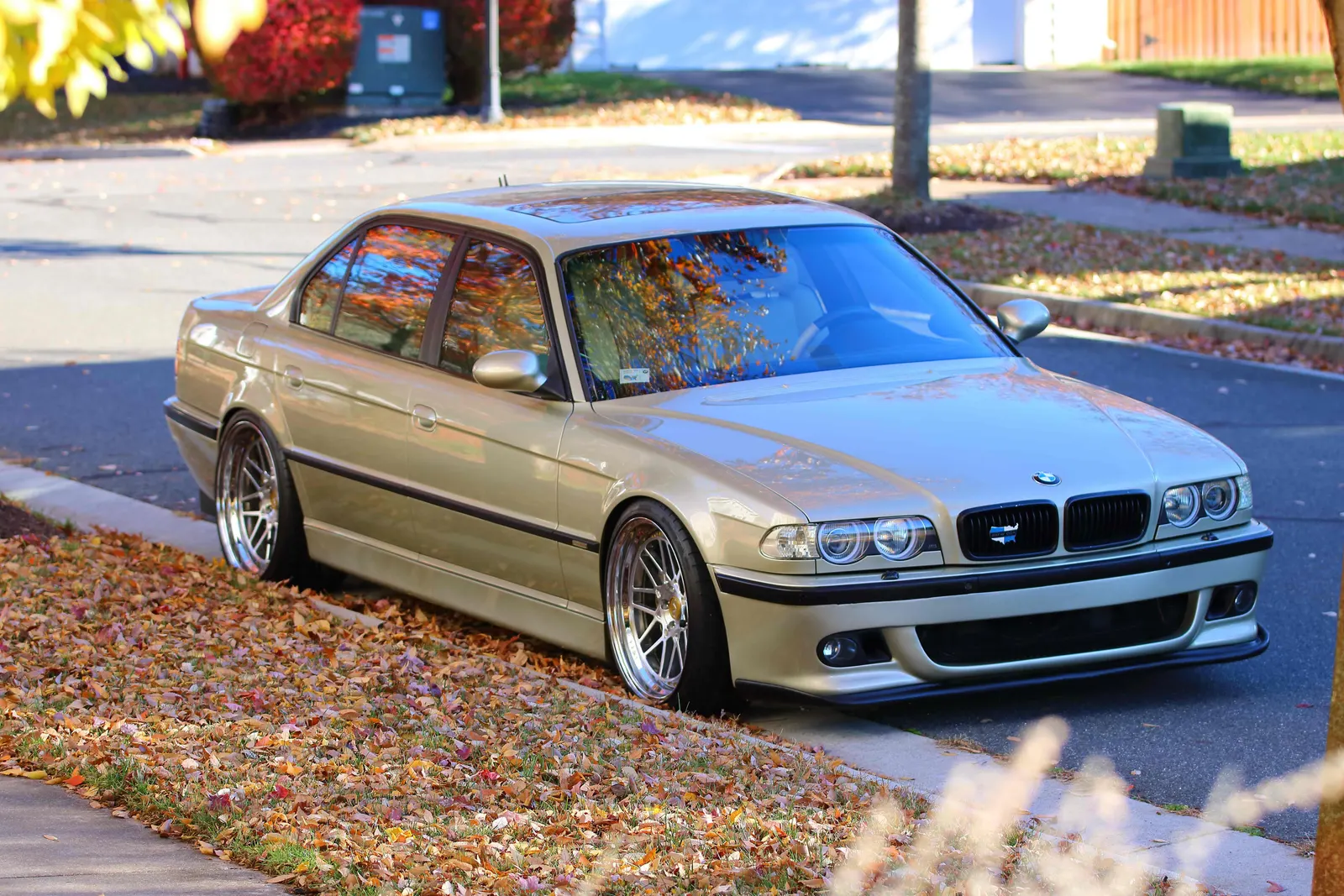 Lowered champagne BMW E38 7 Series on polished multi-spoke wheels parked on an autumn street