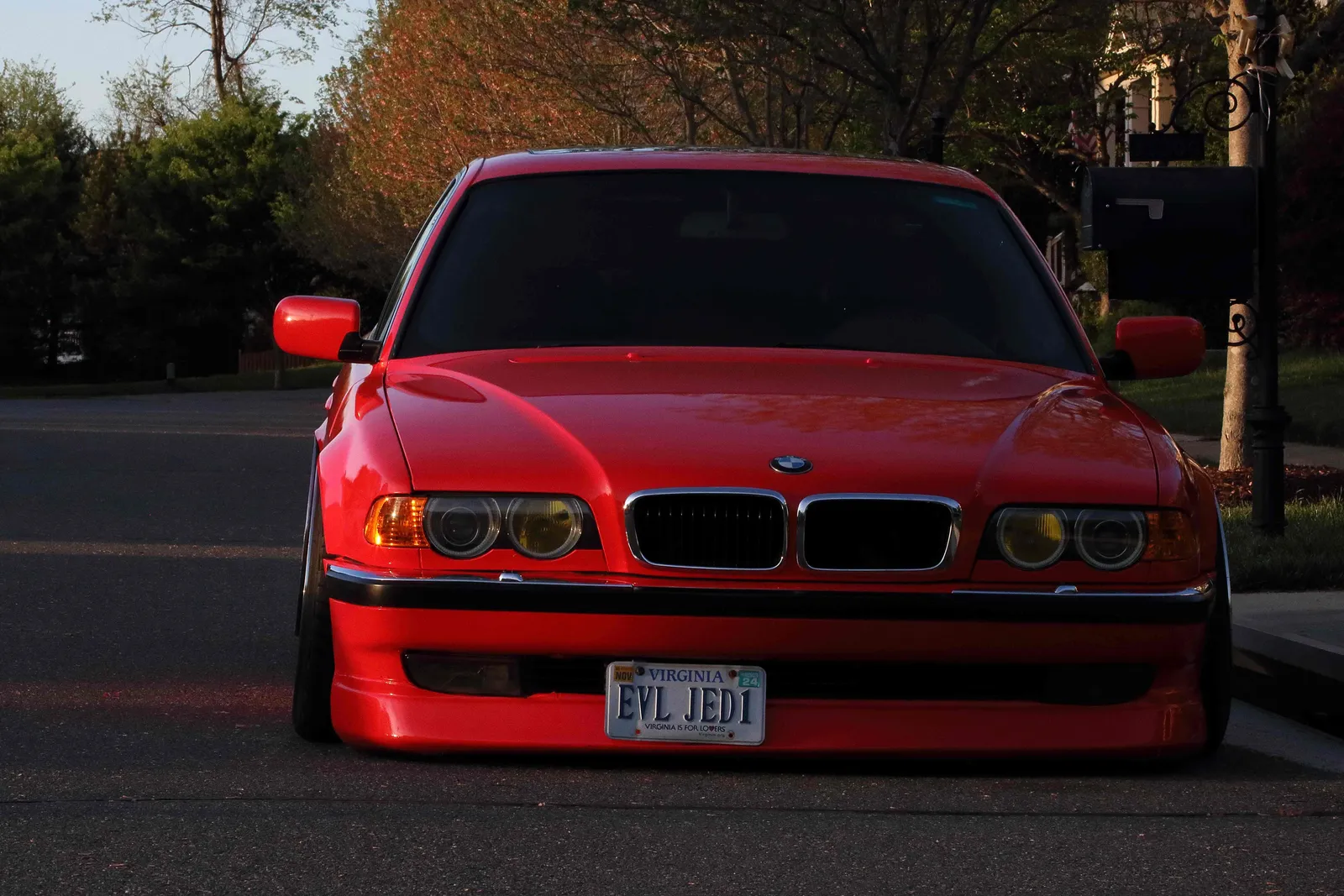 Head-on view of a lowered red BMW E38 7 Series with yellow fog lenses in evening light