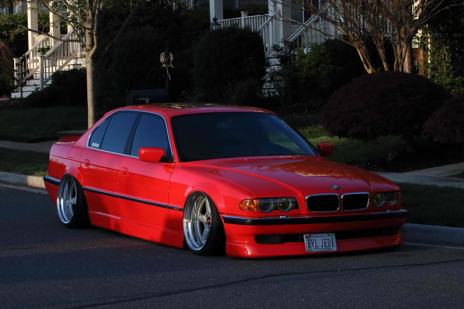 Red BMW E38 7 Series sitting low over polished five-spoke wheels on a residential street at golden hour